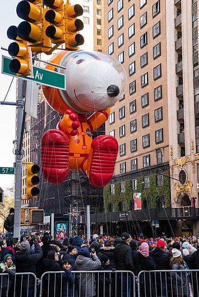 A Snoopy balloon floats down the street during the Macy's Thanksgiving Day Parade. (Anthony Quintano--Public Domain--no changes made--https://commons.wikimedia.org/wiki/File:Macy%27s_Thanksgiving_Day_Parade_2022_New_York_City_%2852523381003%29.jpg)