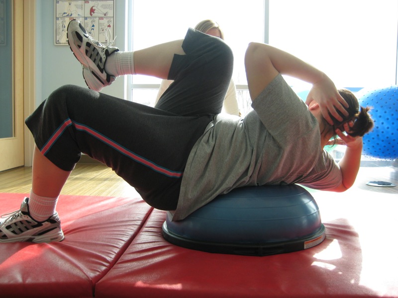 A person completes bicycle crunches on a stability ball over a mat